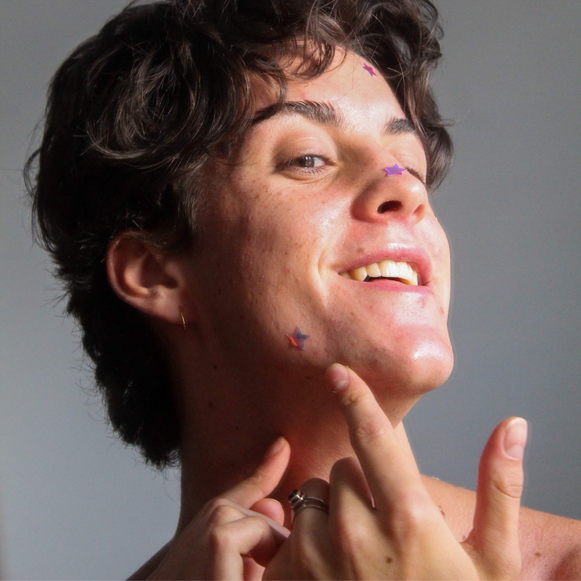 Boy wearing the holographic star shaped pimple patch and also holding a sheet of star pimple patches