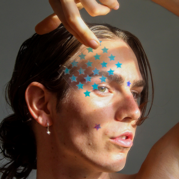 Boy wearing the holographic star acne patch and also holding a sheet of star pimple patches